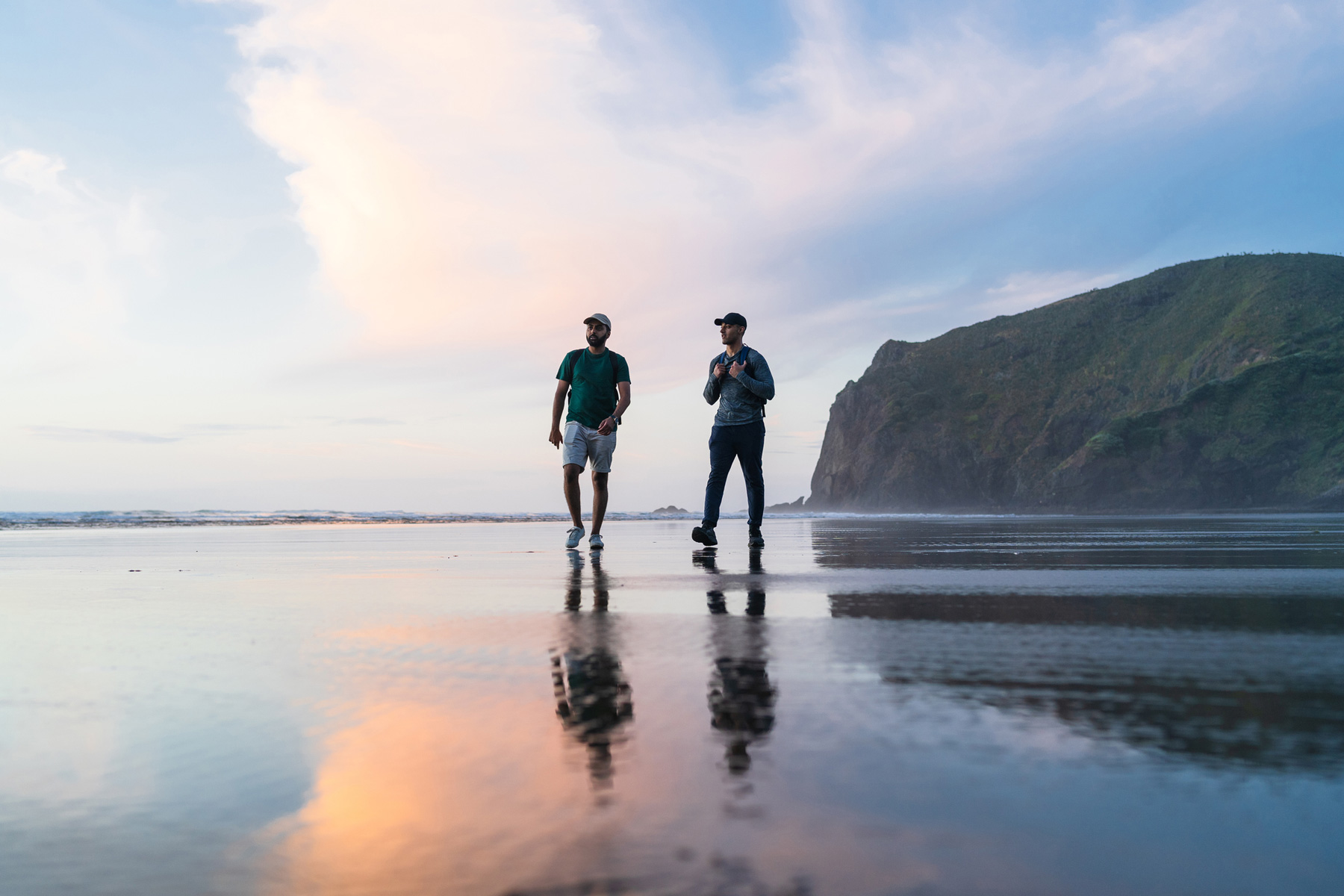 Two people walking on a New Zealand beach at sunset